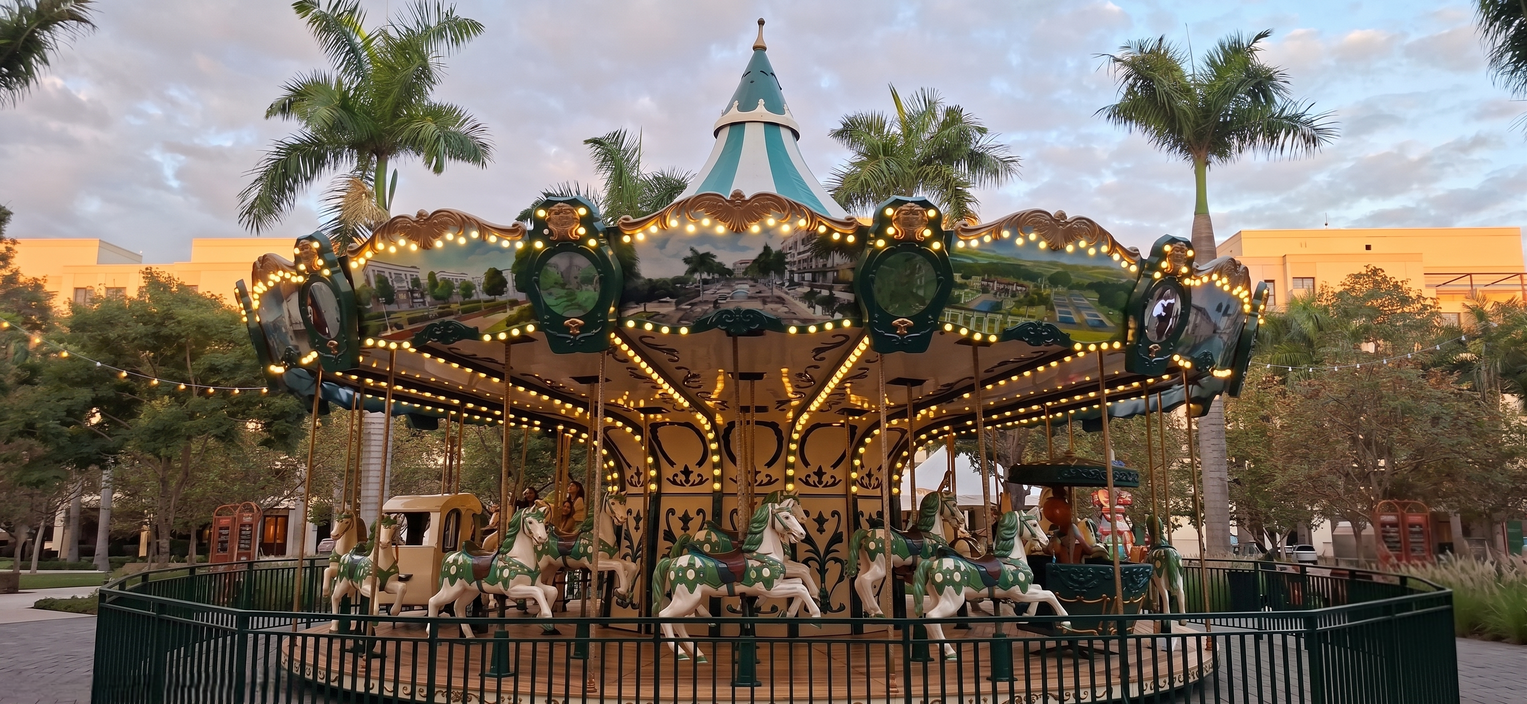 Carrusel iluminado al atardecer, con pinturas en sus cenefas y caballos blancos y verdes